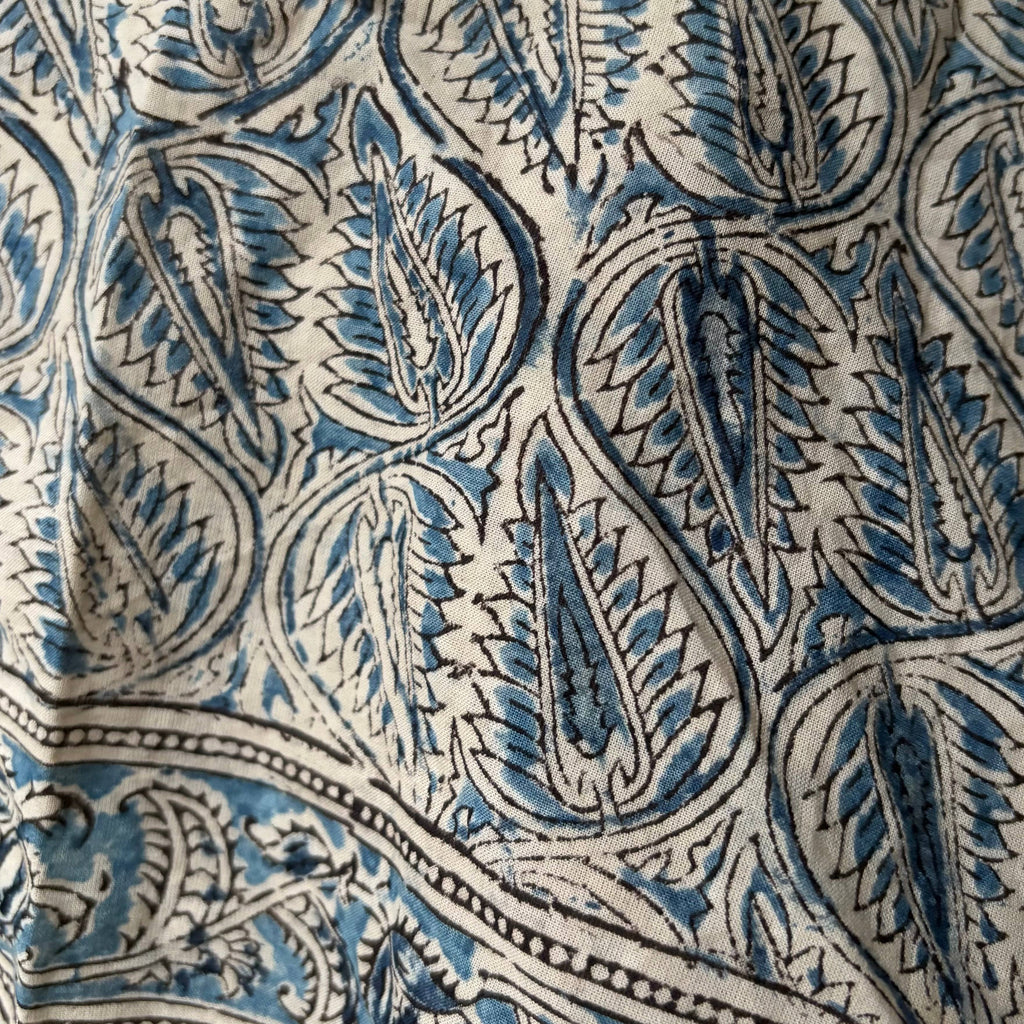 A close-up of a fabric or textile surface with an intricate blue and black paisley block-print pattern on a warm off-white background.