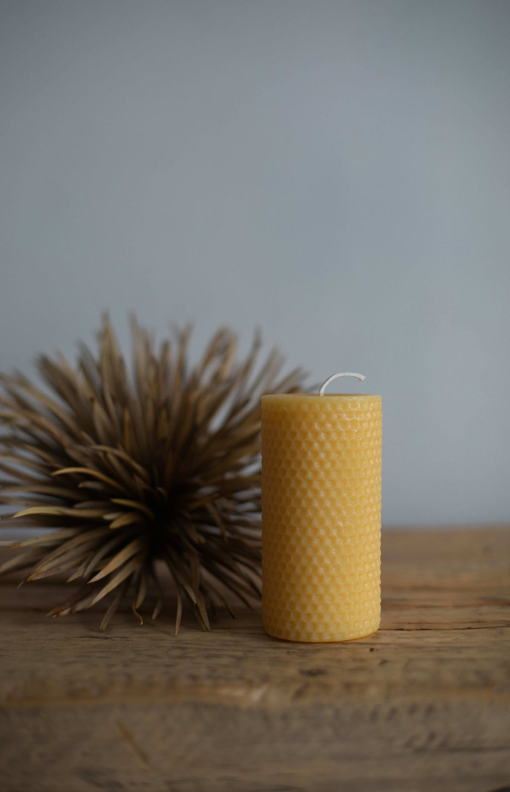 Yellow textured candle on a wooden surface with a blurred plant in the background