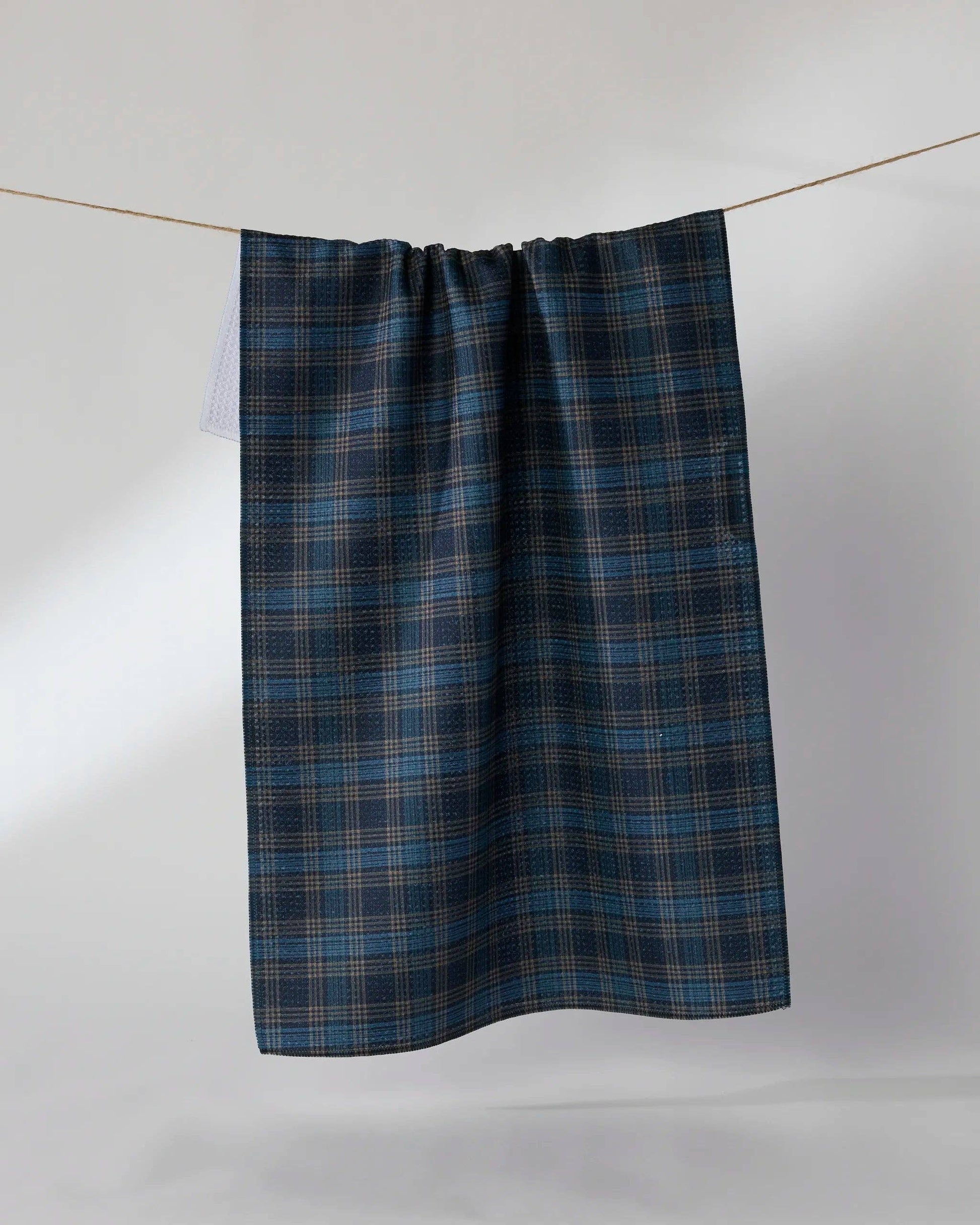 A dark blue and black plaid kitchen towel hanging from a thin wire against a light gray background.