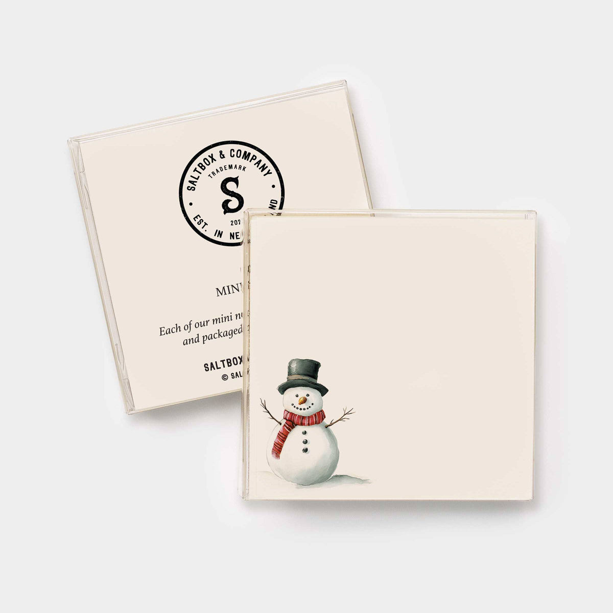 Two cream-colored mini gift boxes from Saltbox & Company, one showing the printed black circular logo and the other featuring a watercolor illustration of a snowman wearing a black top hat and red scarf.