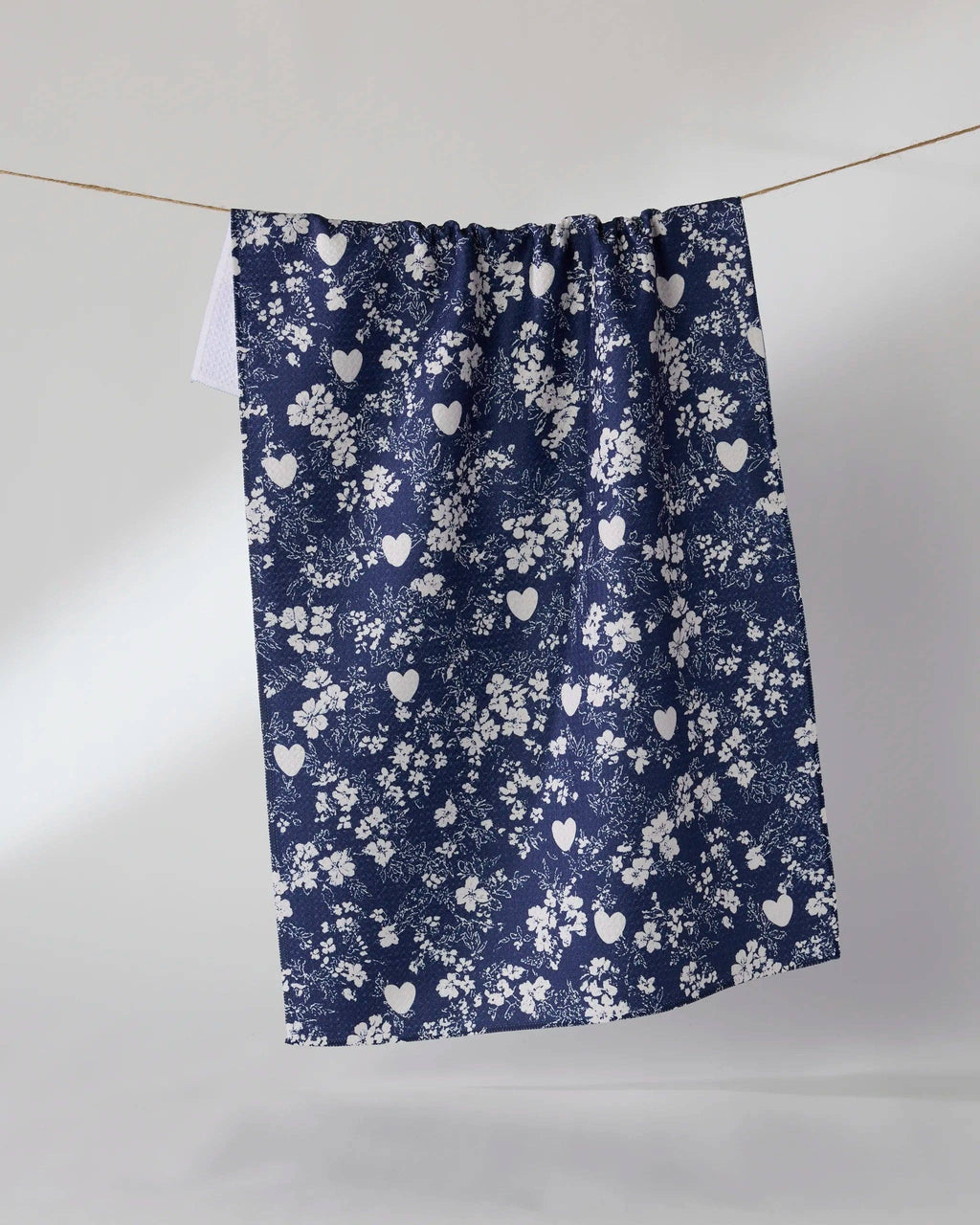 A navy blue curtain panel with a white floral and heart pattern, hanging from a thin wire against a plain light gray studio background.