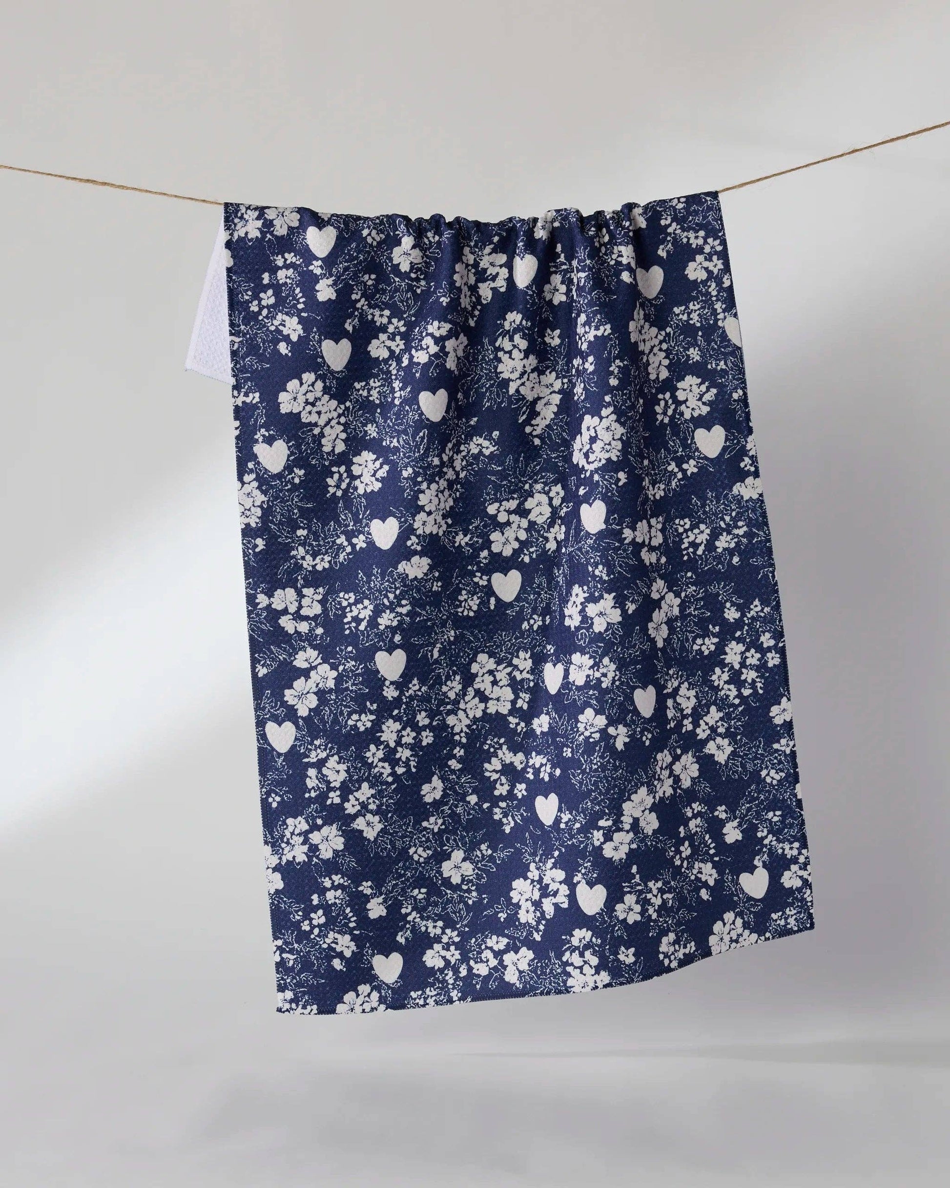A navy blue curtain panel with a white floral and heart pattern, hanging from a thin wire against a plain light gray studio background.