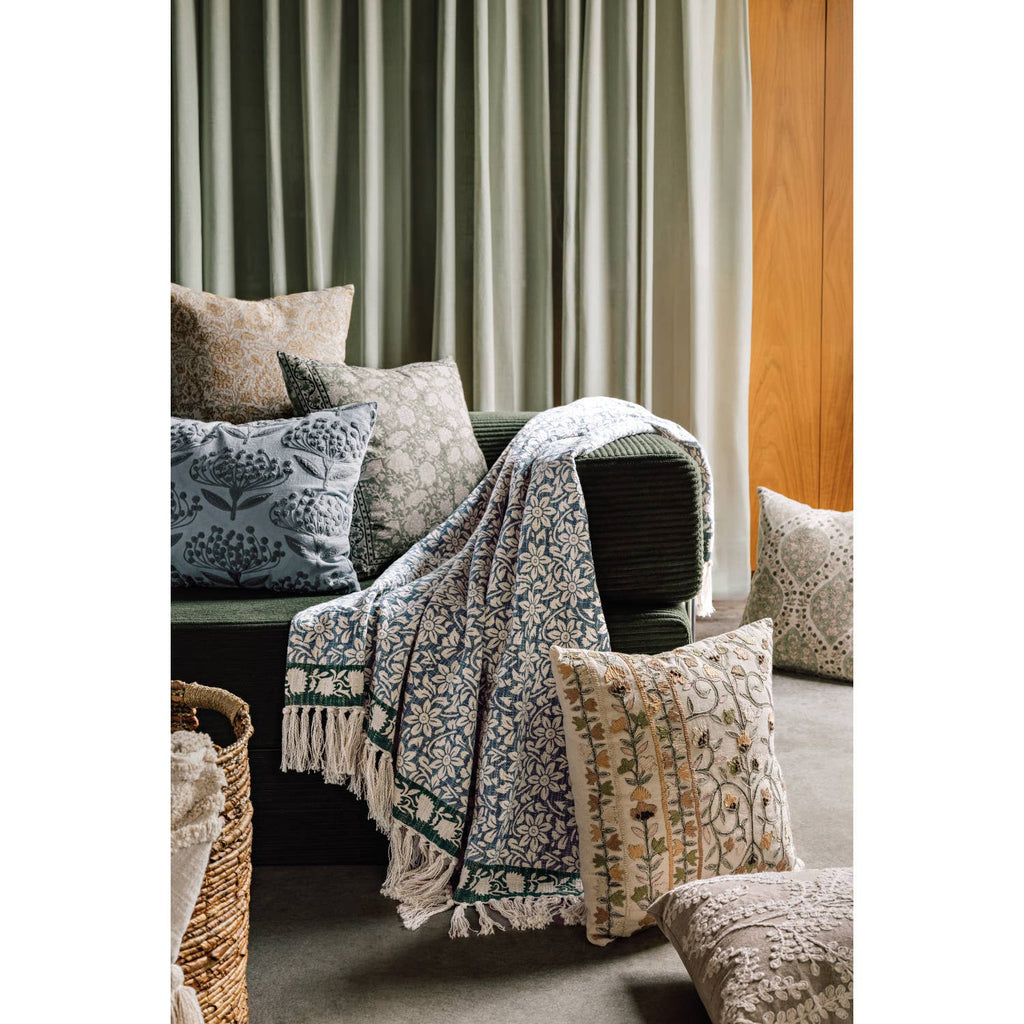 Decorative pillows and blanket on a sofa with curtains in the background