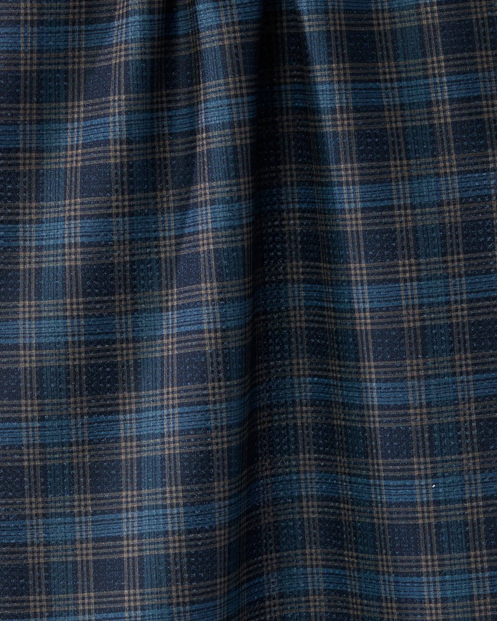 A close-up of a plaid fabric pattern in navy blue, medium blue, and beige, showing the texture and weave of the material.