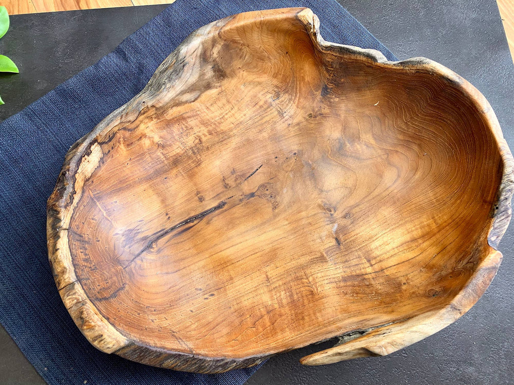 A rustic live-edge wooden bowl with a rich natural grain pattern, resting on a dark blue textured cloth over a dark surface.