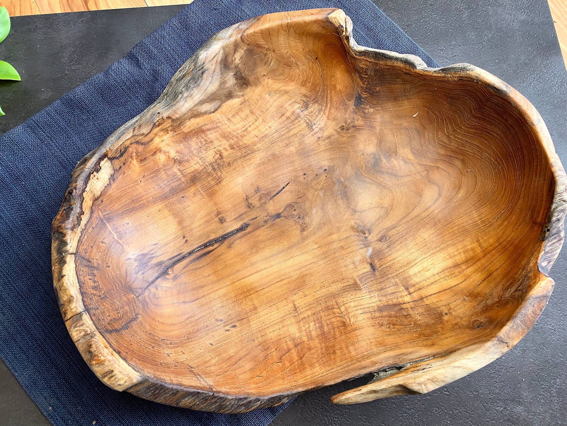 A rustic live-edge wooden bowl with a rich natural grain pattern, resting on a dark blue textured cloth over a dark surface.