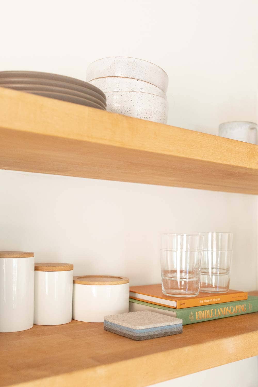 Wooden shelves with kitchen items including jars, a bowl, and books on a white background