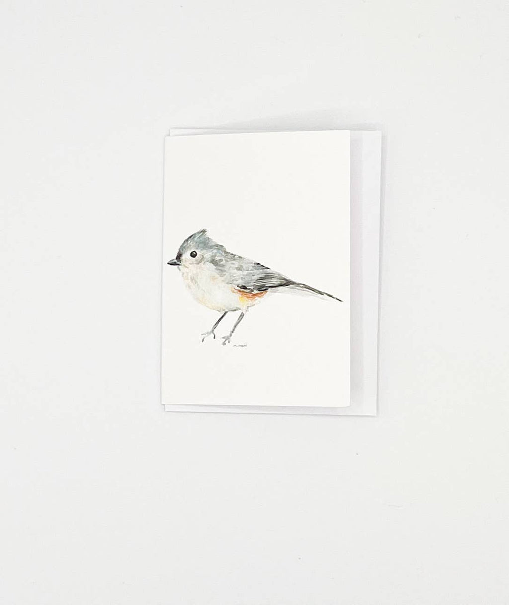 A minimalist greeting card featuring a watercolor illustration of a gray and white bird with a small orange accent, shown with its white envelope against a clean white background.