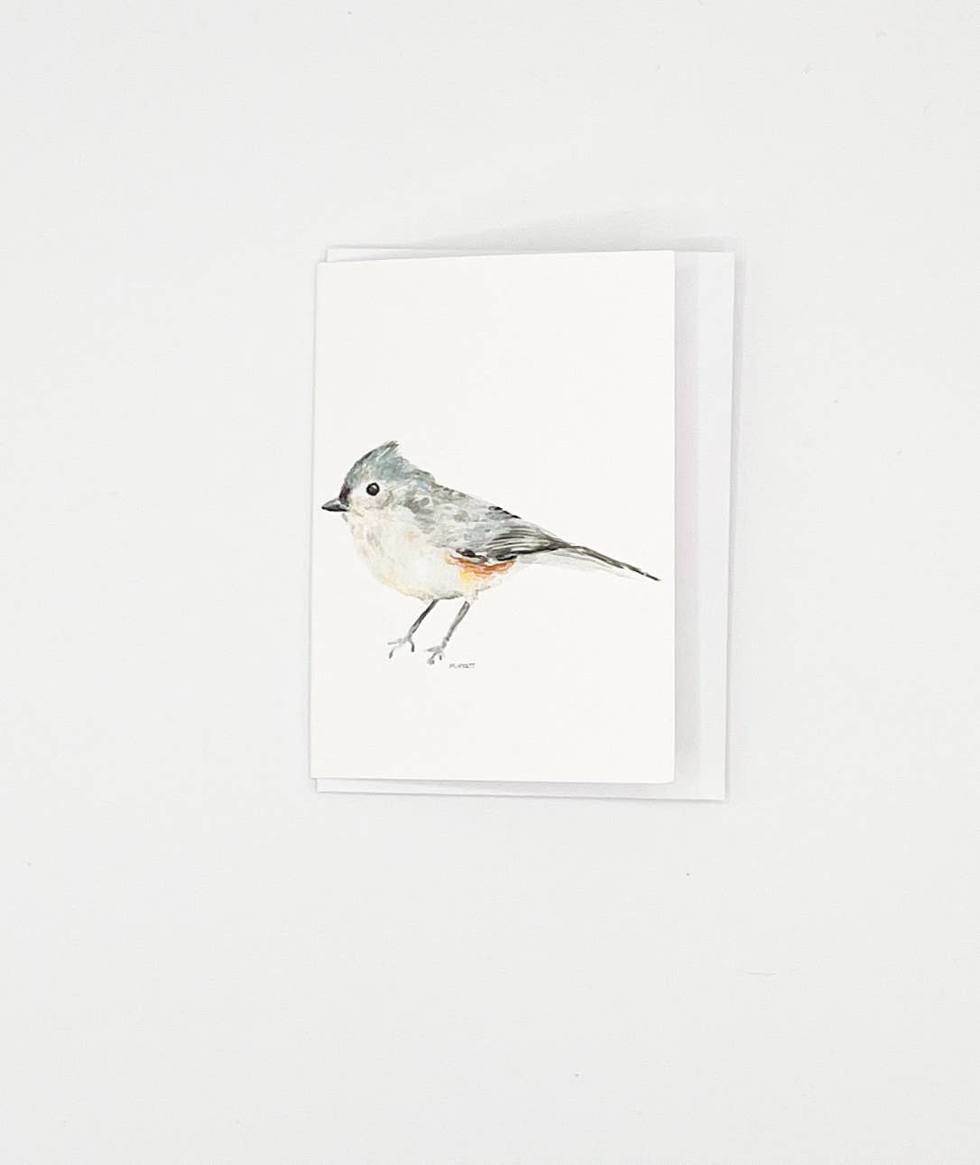 A minimalist greeting card featuring a watercolor illustration of a gray and white bird with a small orange accent, shown with its white envelope against a clean white background.