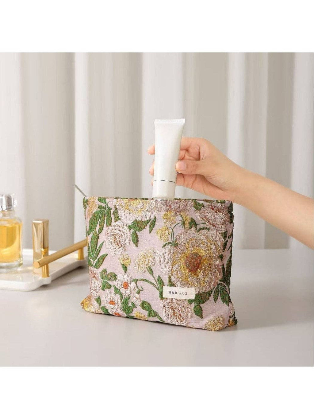Floral-patterned pouch with a hand holding a tube of cream against a neutral background
