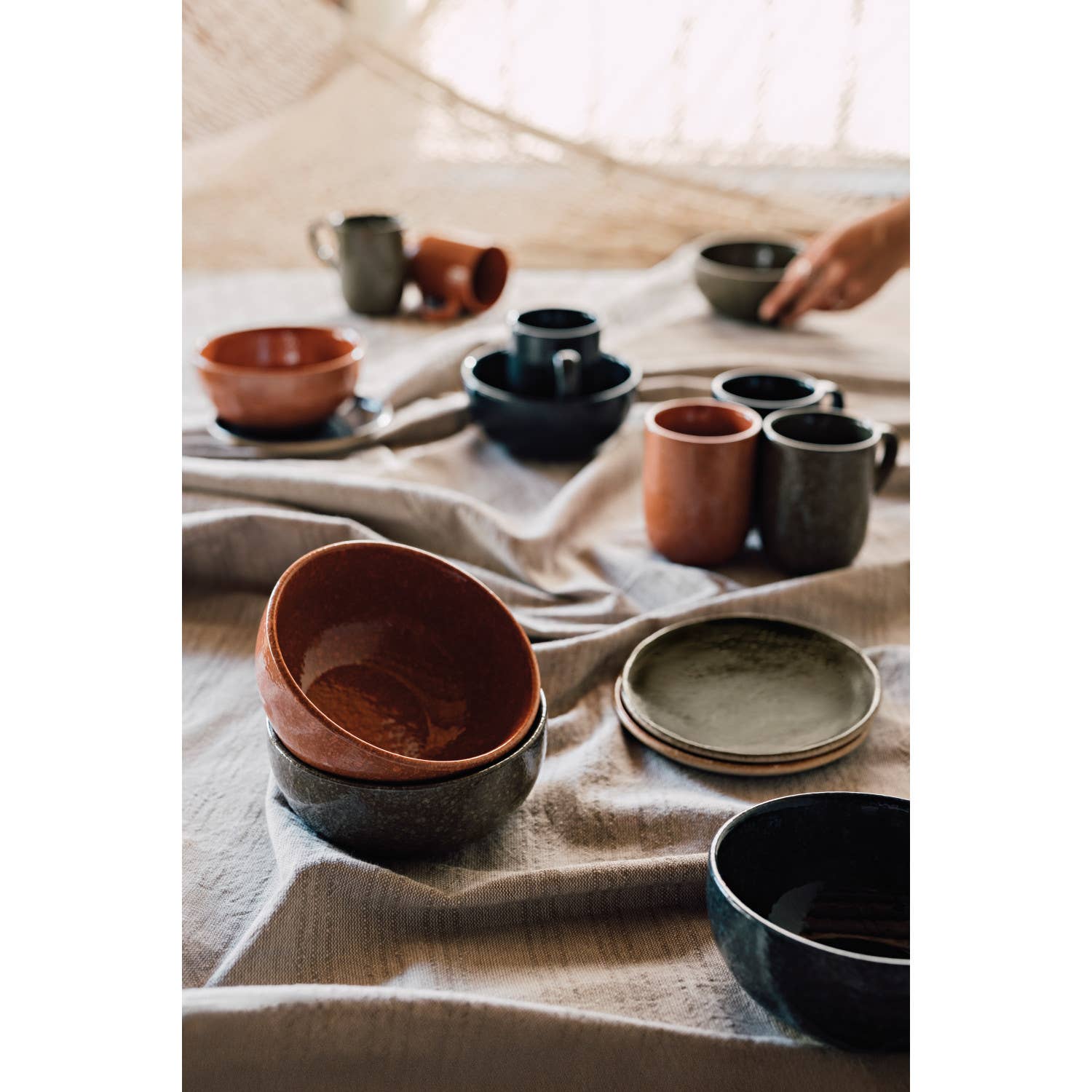 Collection of ceramic bowls and cups on a textured fabric surface