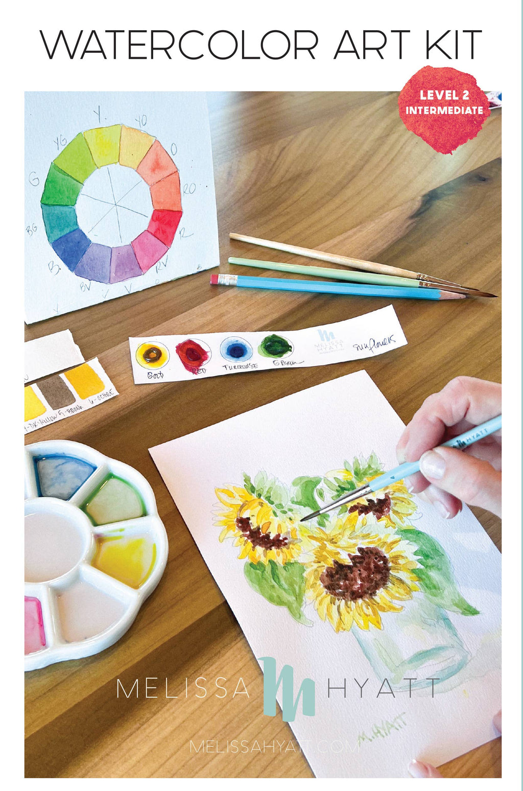 Watercolor art kit shown on a wooden table with a hand painting a sunflower, plus a color wheel, paint tubes, brushes, and a watercolor palette. Text at the top reads 'WATERCOLOR ART KIT' and 'LEVEL 2 INTERMEDIATE'.