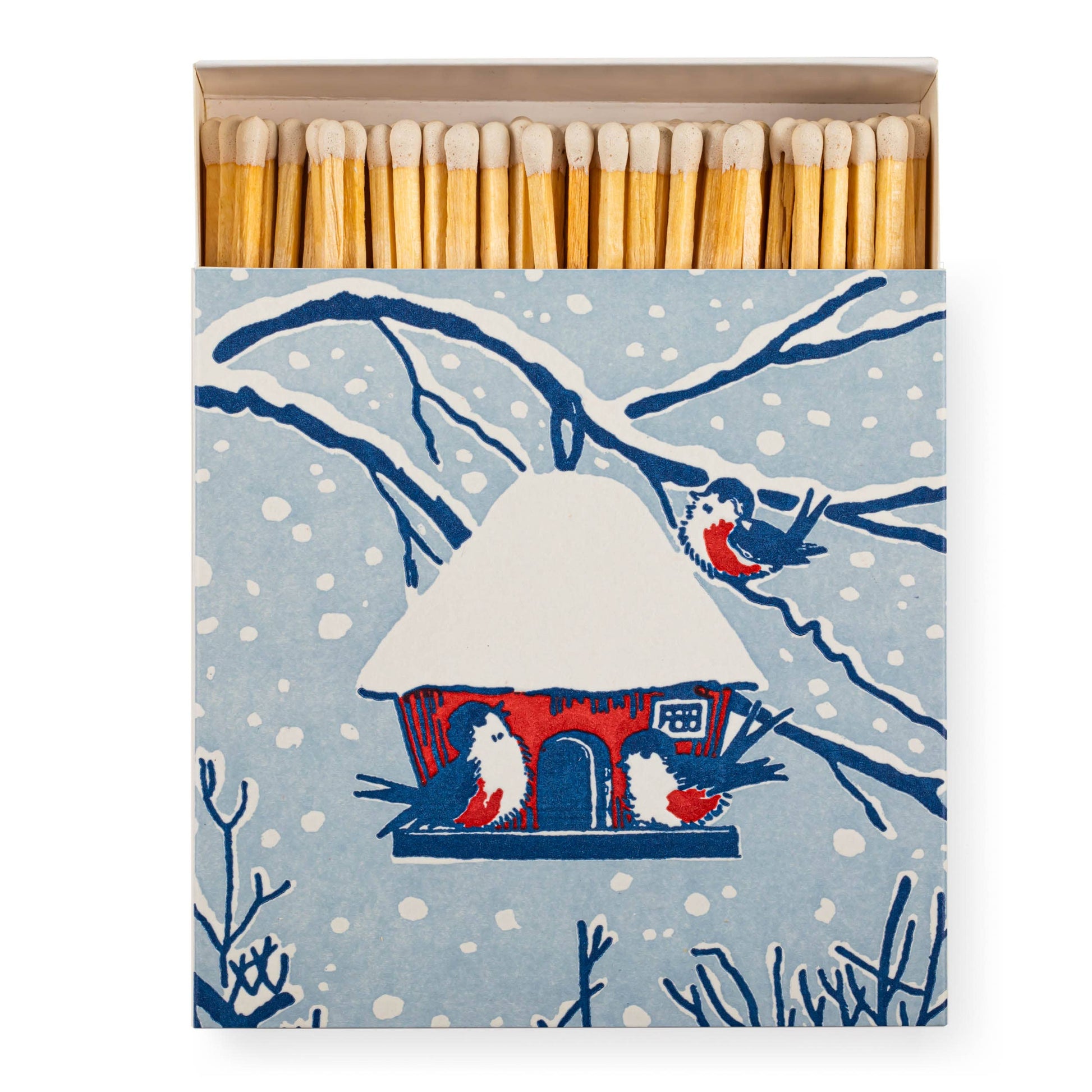 A matchbox with a winter birdhouse illustration on the front, shown open with wooden matches visible. The box features a light blue snowy background with dark blue branches, white birdhouse details, and red accents, plus small birds.