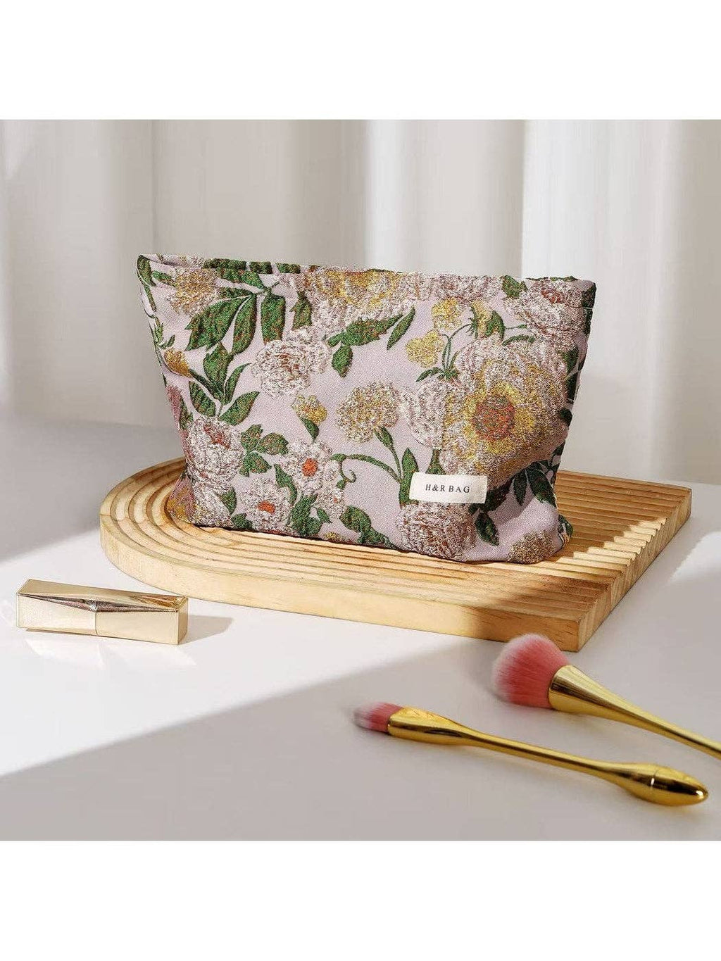 Floral-patterned makeup bag on a wooden tray with cosmetic items on a light surface.