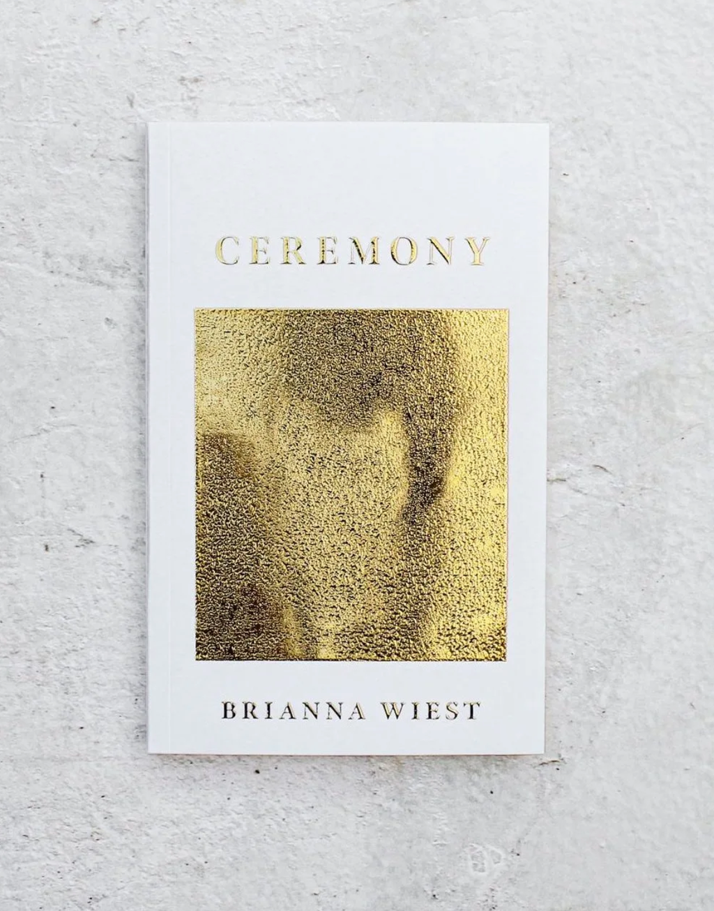 Book titled 'Ceremony' by Brianna Wiest with gold cover on a light gray background