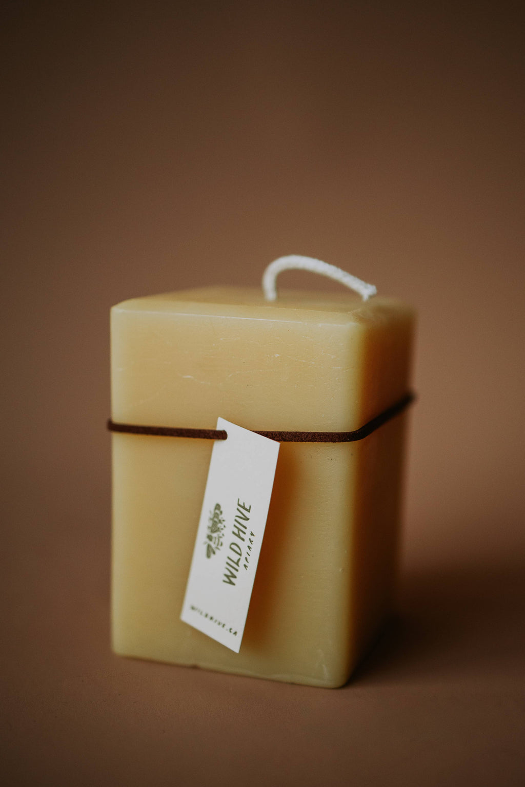 Square beeswax candle with a visible brand tag on a brown background