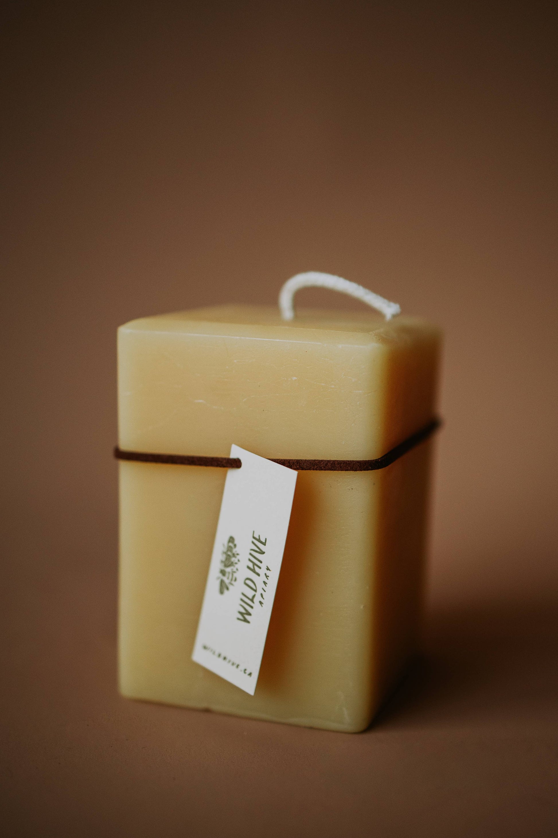 Square beeswax candle with a visible brand tag on a brown background