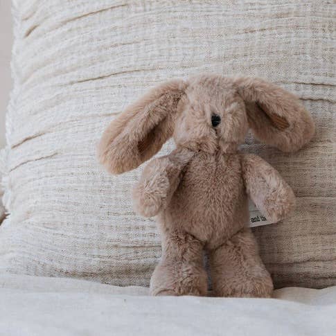 Plush bunny toy with a tag on a textured beige background