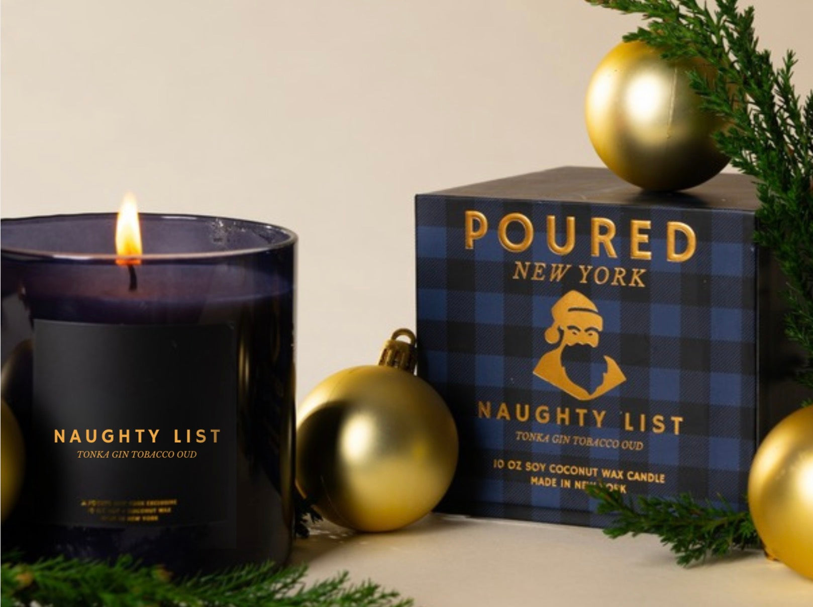 A lit dark purple candle labeled 'NAUGHTY LIST' sits beside its branded box, styled with gold ornaments and evergreen branches on a light neutral background.