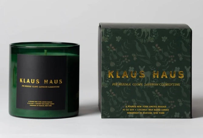 A dark green glass candle jar with a black label next to its matching dark green box with gold lettering, both branded Klaus Haus.