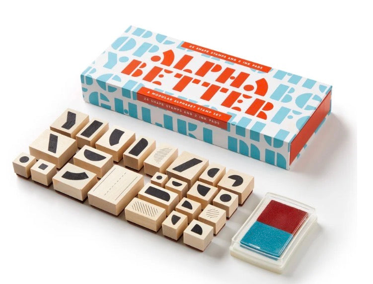 An alphabet stamp set with wooden alphabet blocks, a box labeled 'Alpha Better', and a small ink pad on a clean white background.