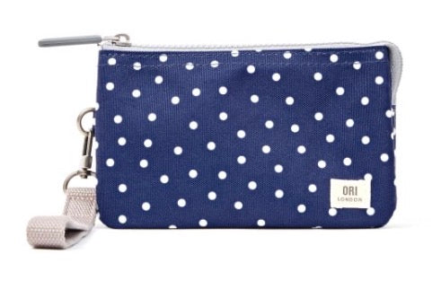 A navy blue canvas wristlet pouch with white polka dots, featuring a silver zipper, a light beige fabric wrist strap, and a small white brand label on the bottom right.