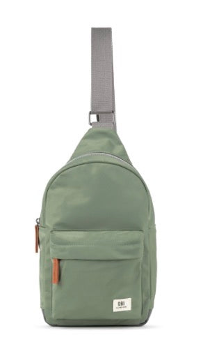 An olive green sling backpack with a gray adjustable shoulder strap, featuring a front zippered pocket with a small white brand label.