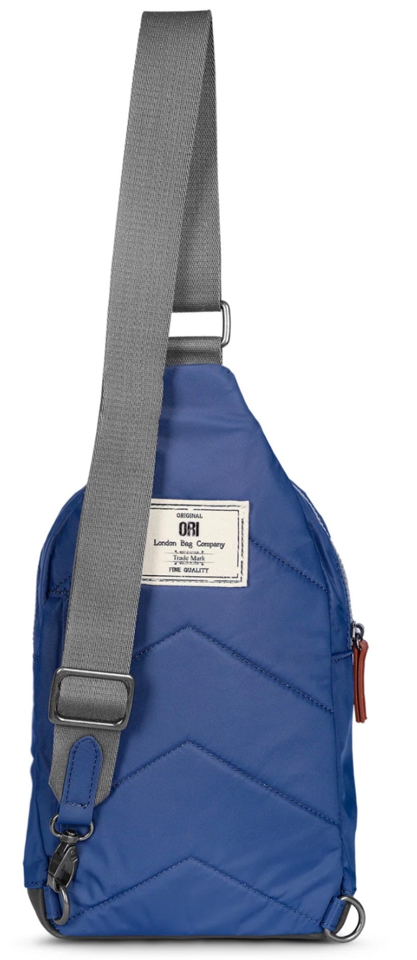 A blue sling backpack with a gray adjustable shoulder strap, featuring a white brand label that reads 'GTM Global Tote Company' and a small brown leather zipper pull.