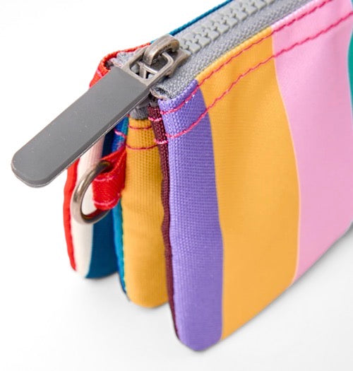A close-up of a small zip pouch with vertical rainbow-colored stripes in pink, yellow, purple, blue, and red, featuring a gray zipper pull and silver metal hardware.
