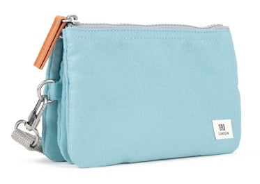 A light blue canvas pouch with a silver zipper, a brown leather pull tab, and a small white brand label on the bottom right corner, set against a plain white background.