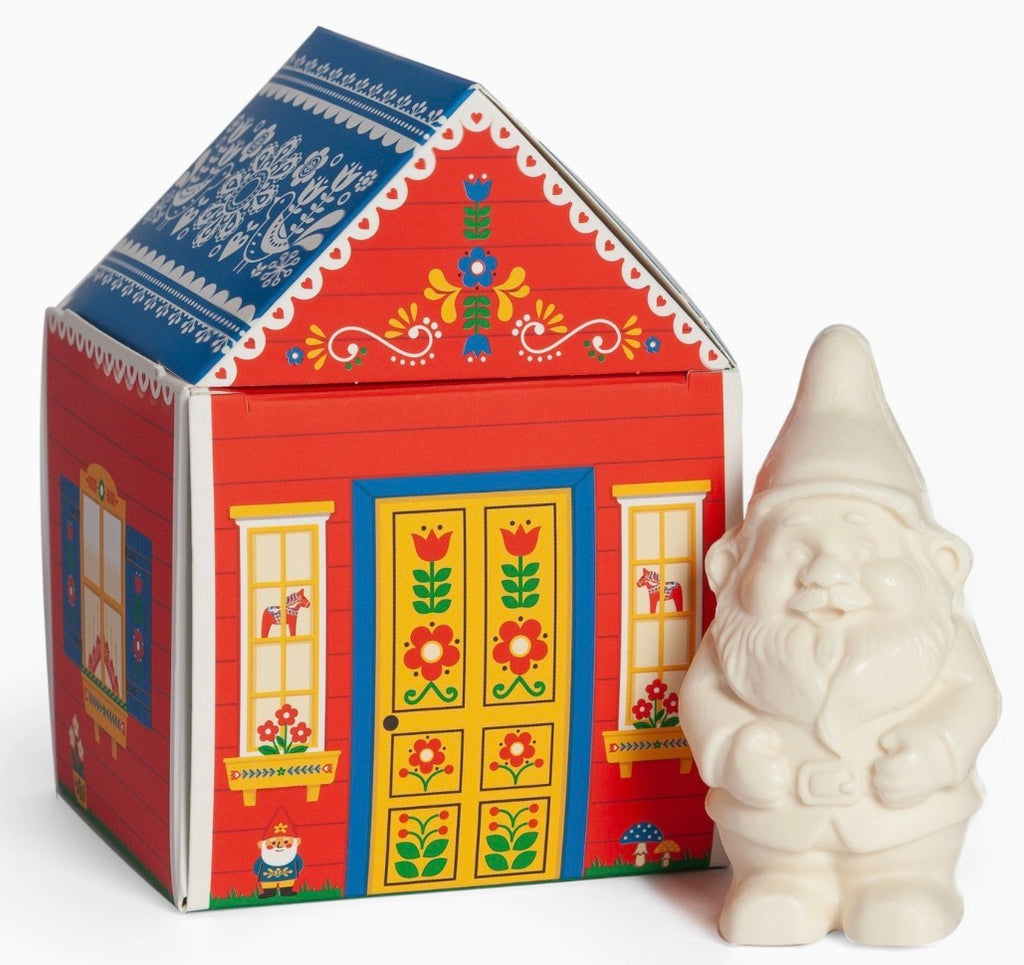 A red house-shaped gift box with colorful floral and geometric patterns, shown next to a small off-white gnome figurine on a plain white background.