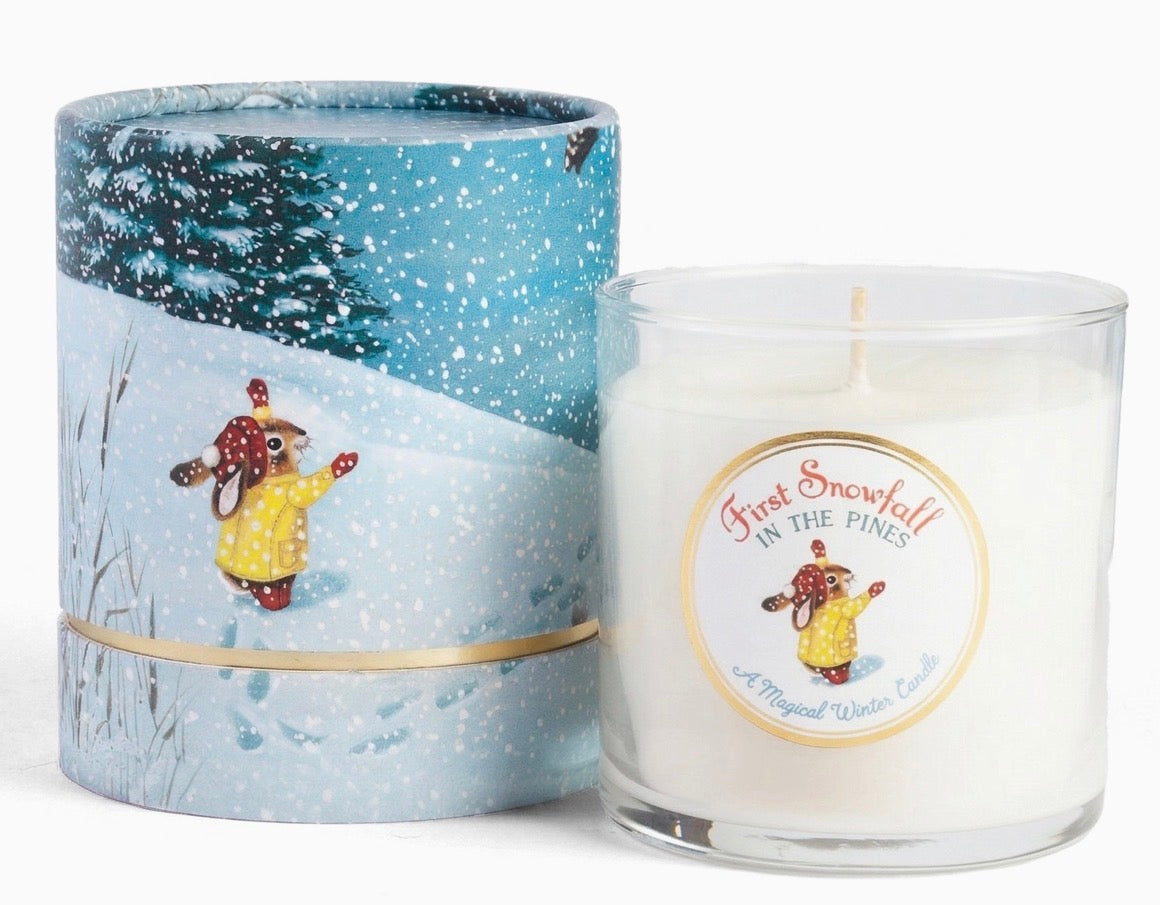 A scented winter candle shown with its matching cylindrical tin packaging. The tin features a winter illustration of a rabbit in a yellow coat walking through a snowy landscape under a starry night sky.