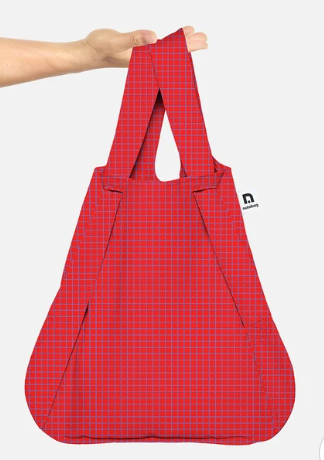 A red reusable tote bag with a fine white grid pattern, held by a person's hand against a light gray background.