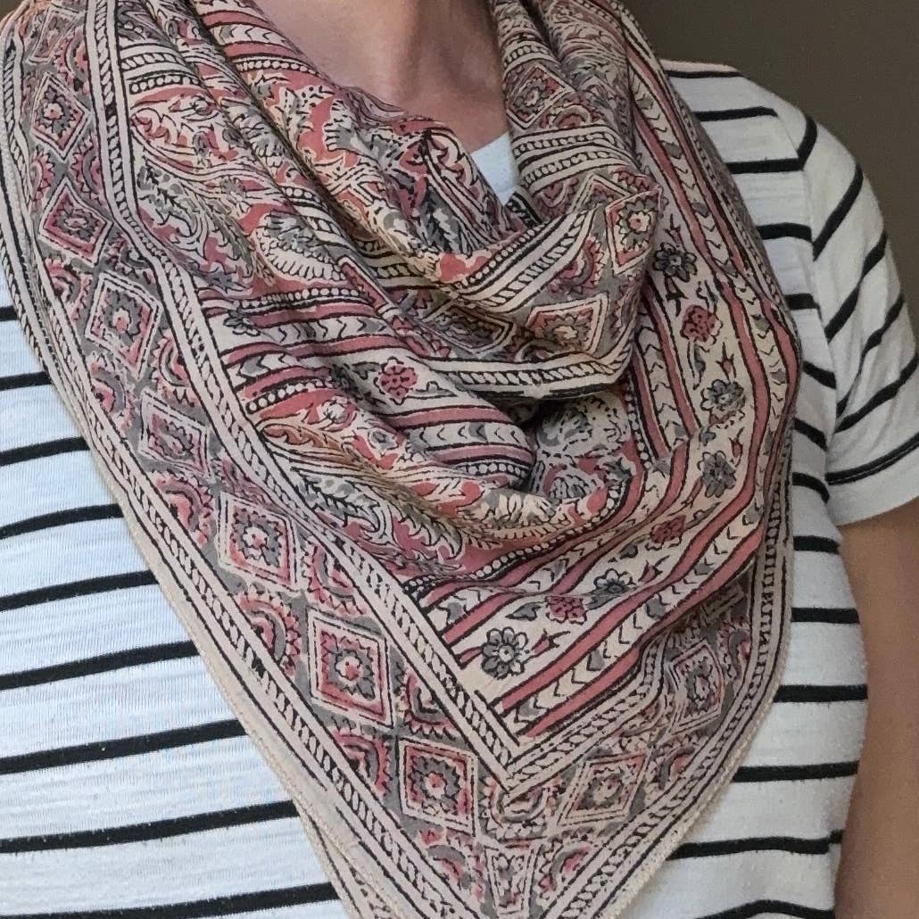 A close-up of a person wearing a large, draped scarf with a detailed geometric and floral pattern in beige, pink, and brown tones over a black and white striped shirt.
