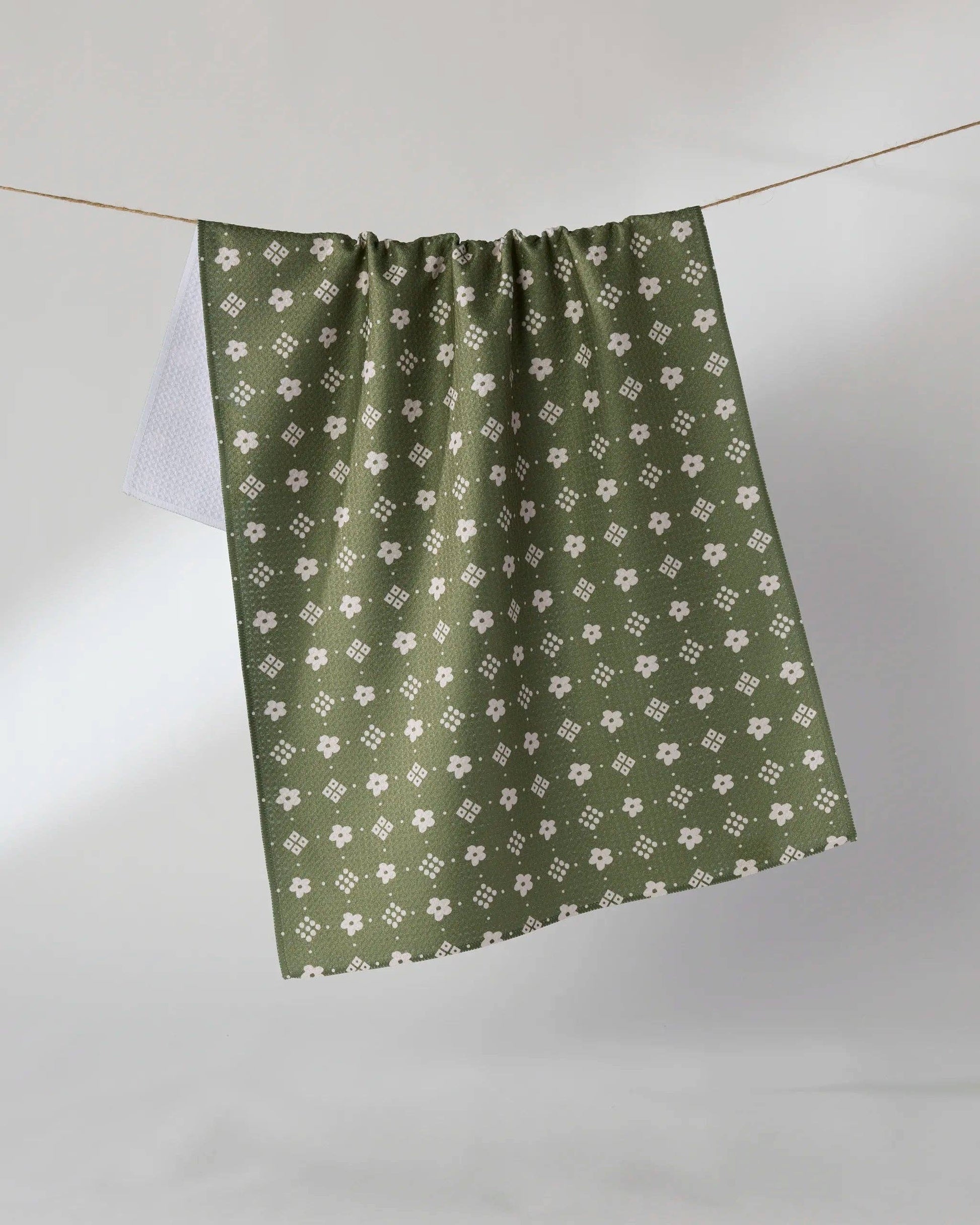 An olive green curtain panel with a repeating white floral and geometric pattern, hanging from a thin wire against a neutral gray background.