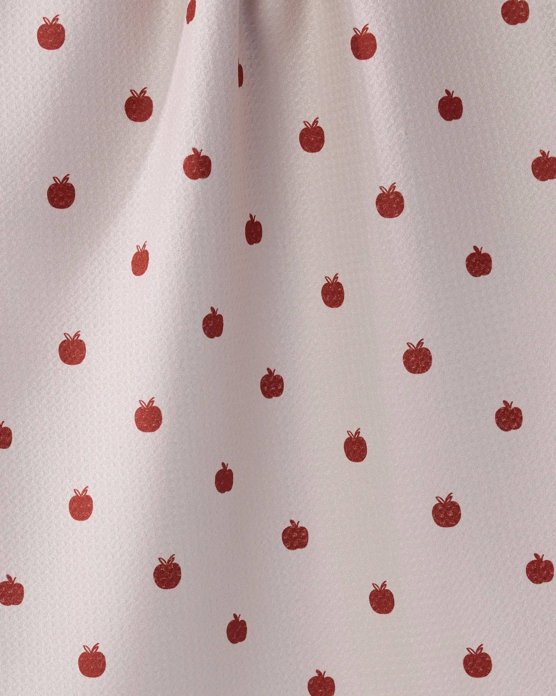 A close-up of a light pink or off-white fabric with a repeating pattern of small red apples.
