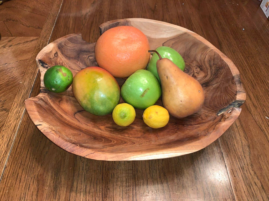 A rustic handcrafted wooden bowl with natural live edges, filled with fresh fruit including a pear, mango, oranges, and limes, set on a wooden table.