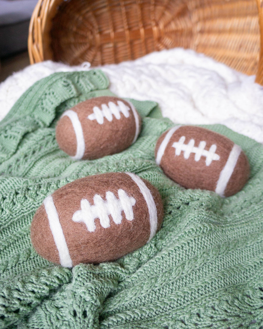 Three brown and white football-shaped objects on a green textured surface with a wicker basket in the background.