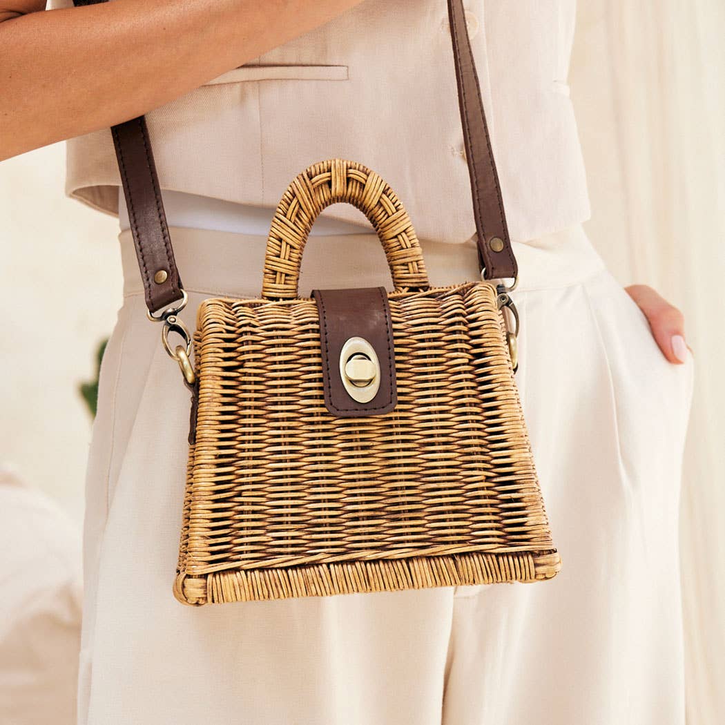 Wicker handbag with brown leather accents held by a person wearing a light-colored outfit.