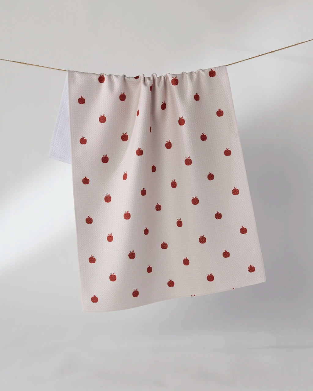 A white kitchen curtain panel with a repeating red strawberry print, hanging from a thin wire on a light gray background.