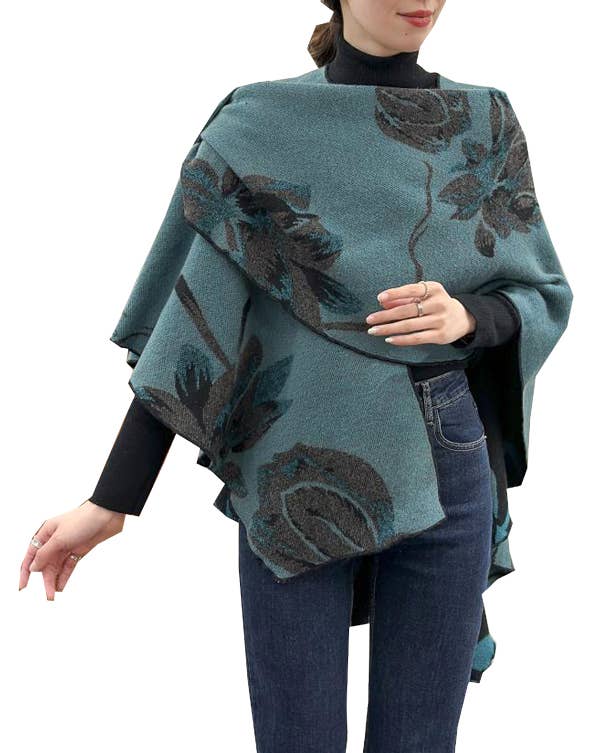A woman wearing a teal blue-green poncho-style wrap with a dark floral pattern, styled over a black turtleneck and blue jeans against a plain white background.