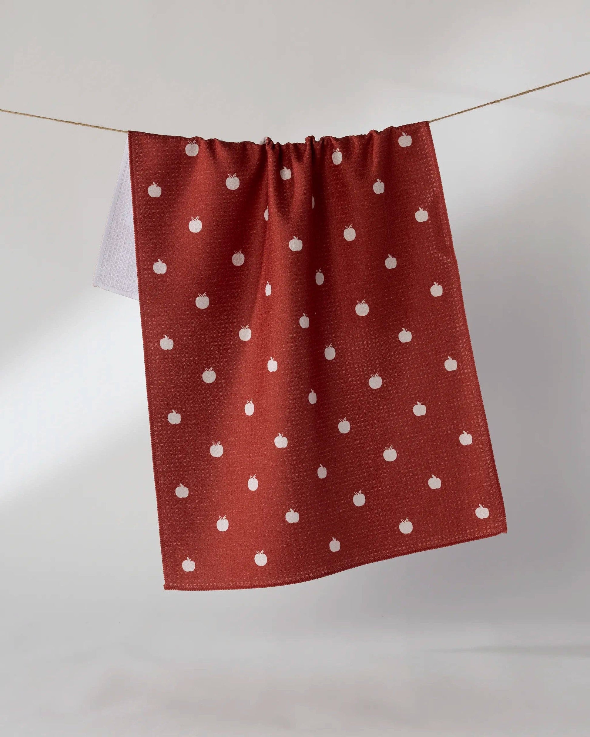 A terracotta red kitchen towel with a white pumpkin pattern, hanging from a string against a light gray background.