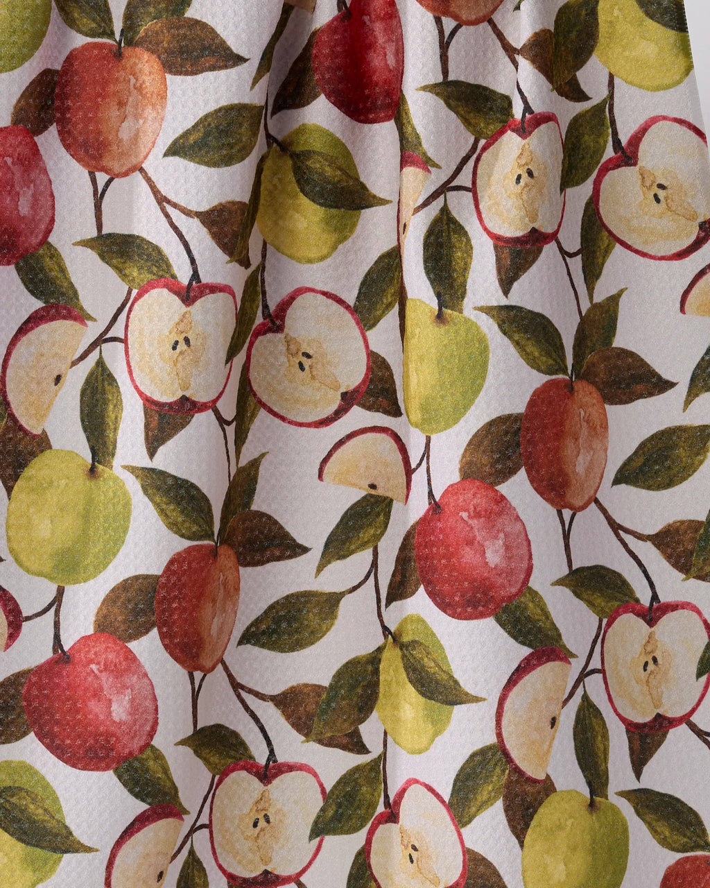 A close-up of a fabric or wallpaper pattern featuring watercolor-style apples in red, yellow-green, and cream, with dark green leaves on a white background.