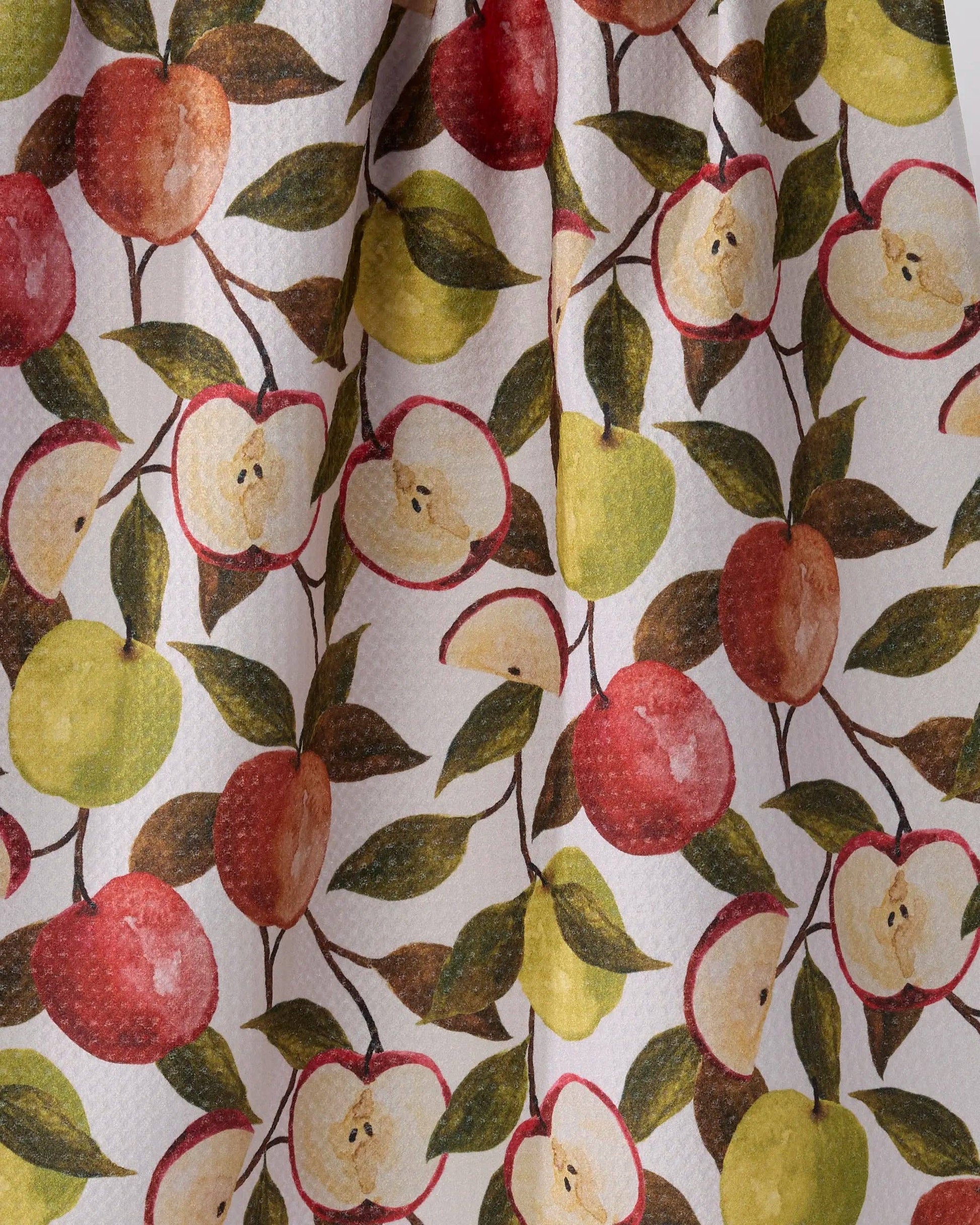 A close-up of a fabric or wallpaper pattern featuring watercolor-style apples in red, yellow-green, and cream, with dark green leaves on a white background.