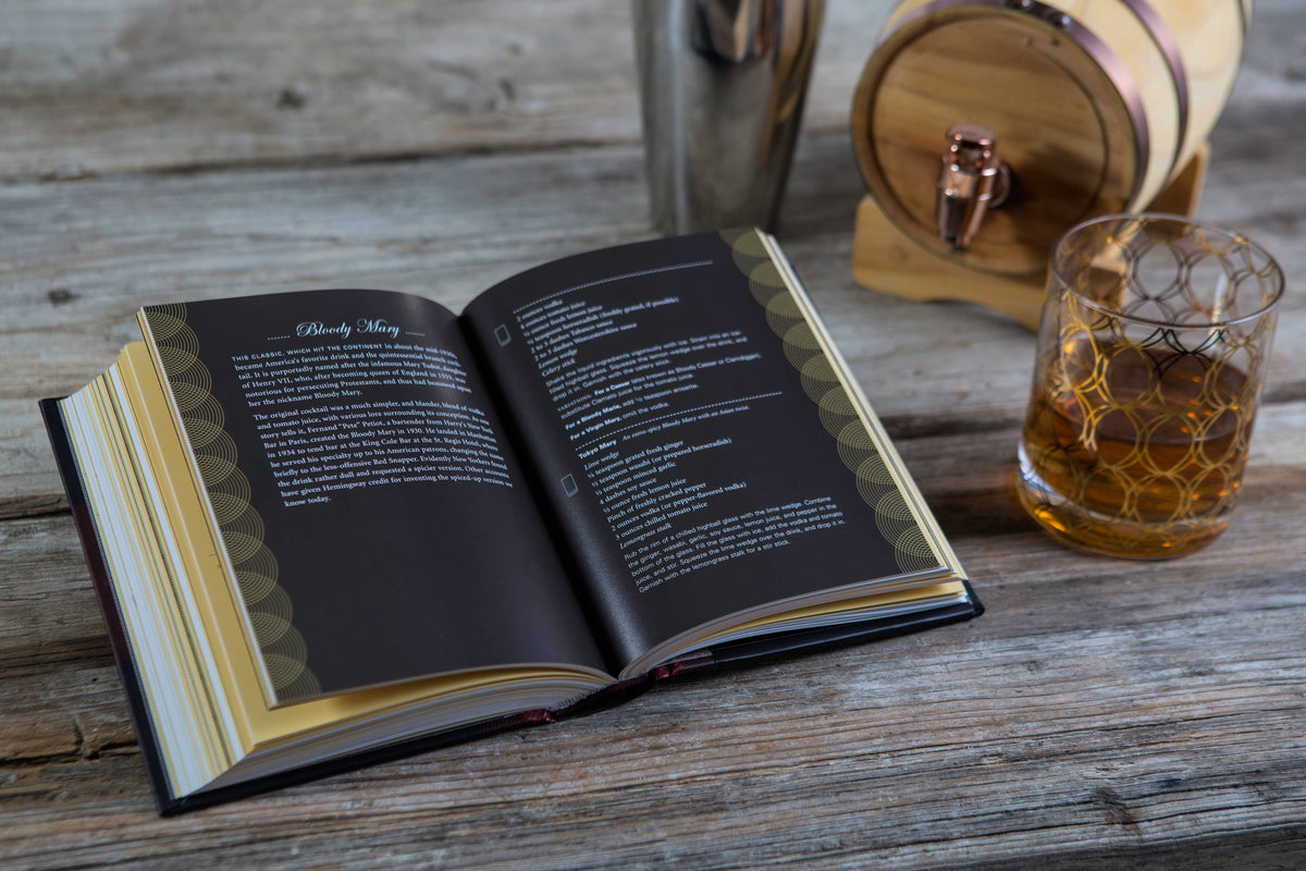Open book on a wooden surface with a glass of whiskey and barrel in the background