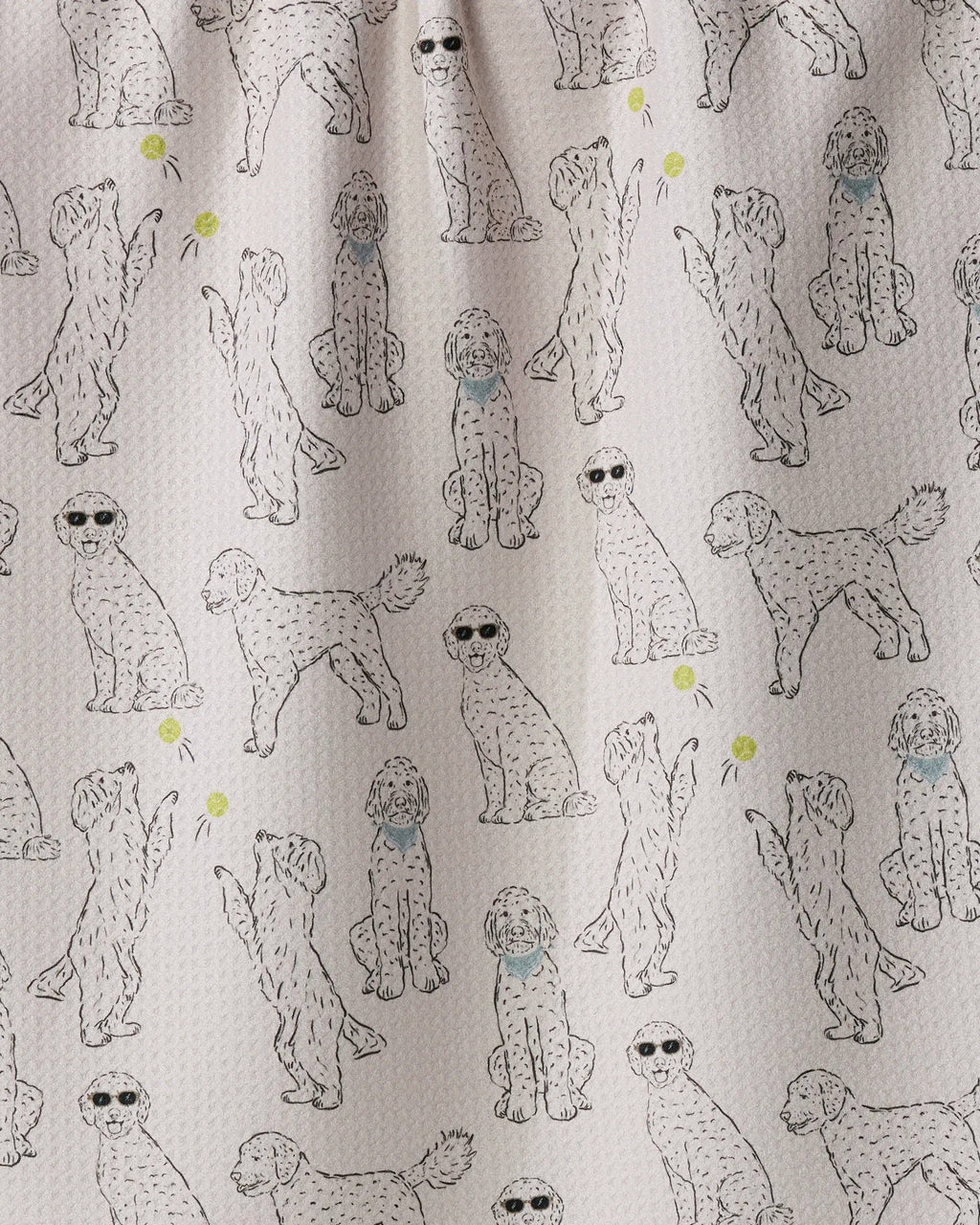 A close-up of a fabric surface with an allover print of doodle-style poodles in light gray and black, with a few small yellow tennis balls and blue bandanas.