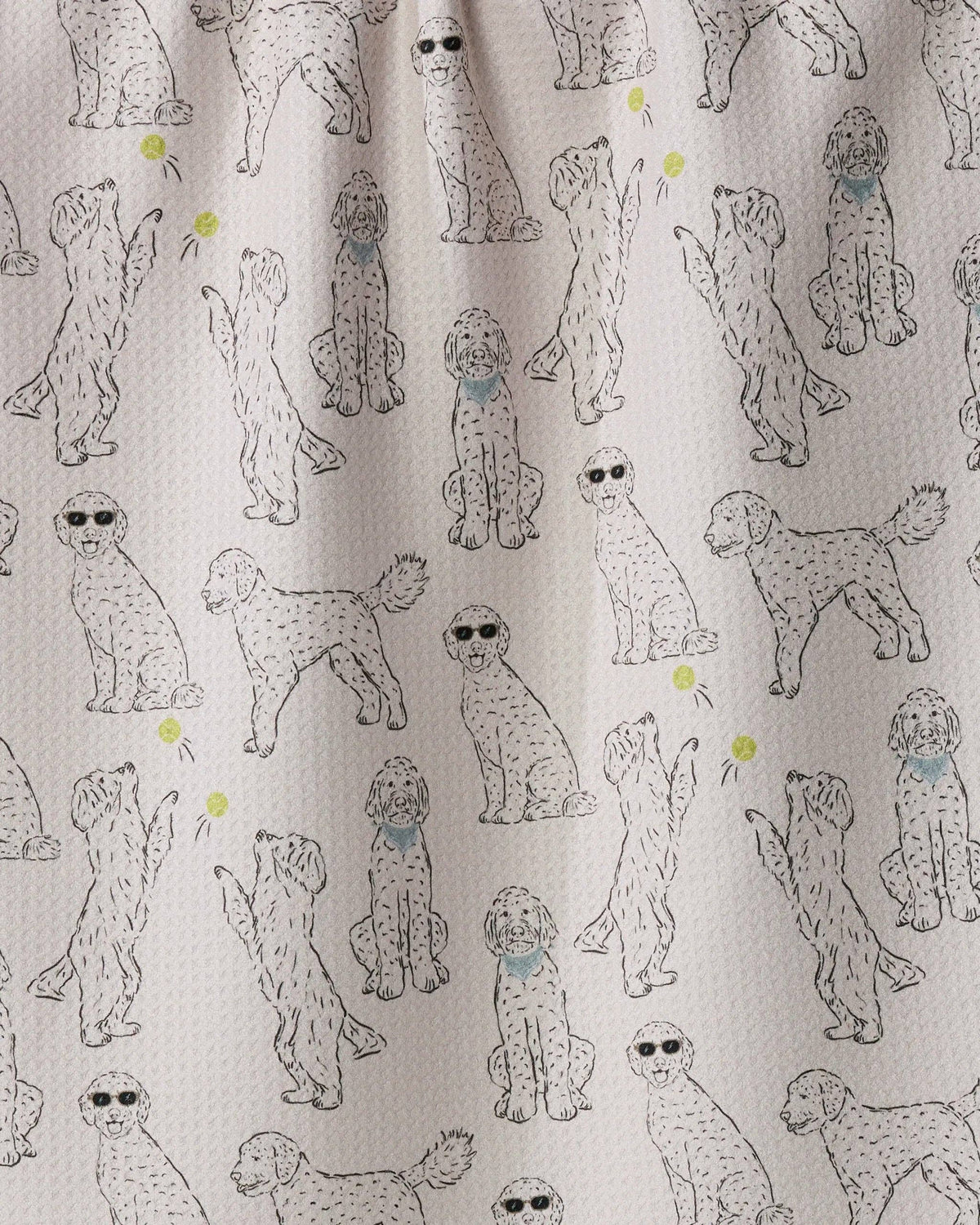 A close-up of a fabric surface with an allover print of doodle-style poodles in light gray and black, with a few small yellow tennis balls and blue bandanas.