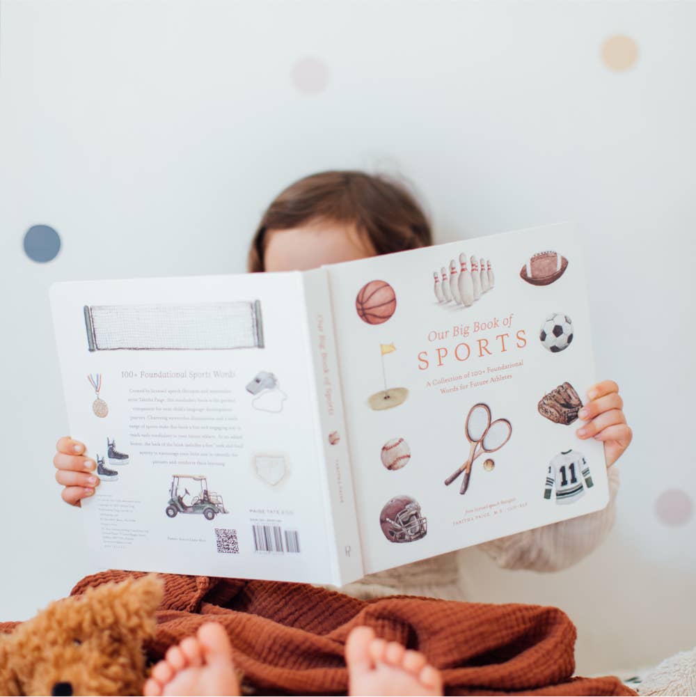Child reading a book titled 'Big Book of Sports' with a soft, blurred background