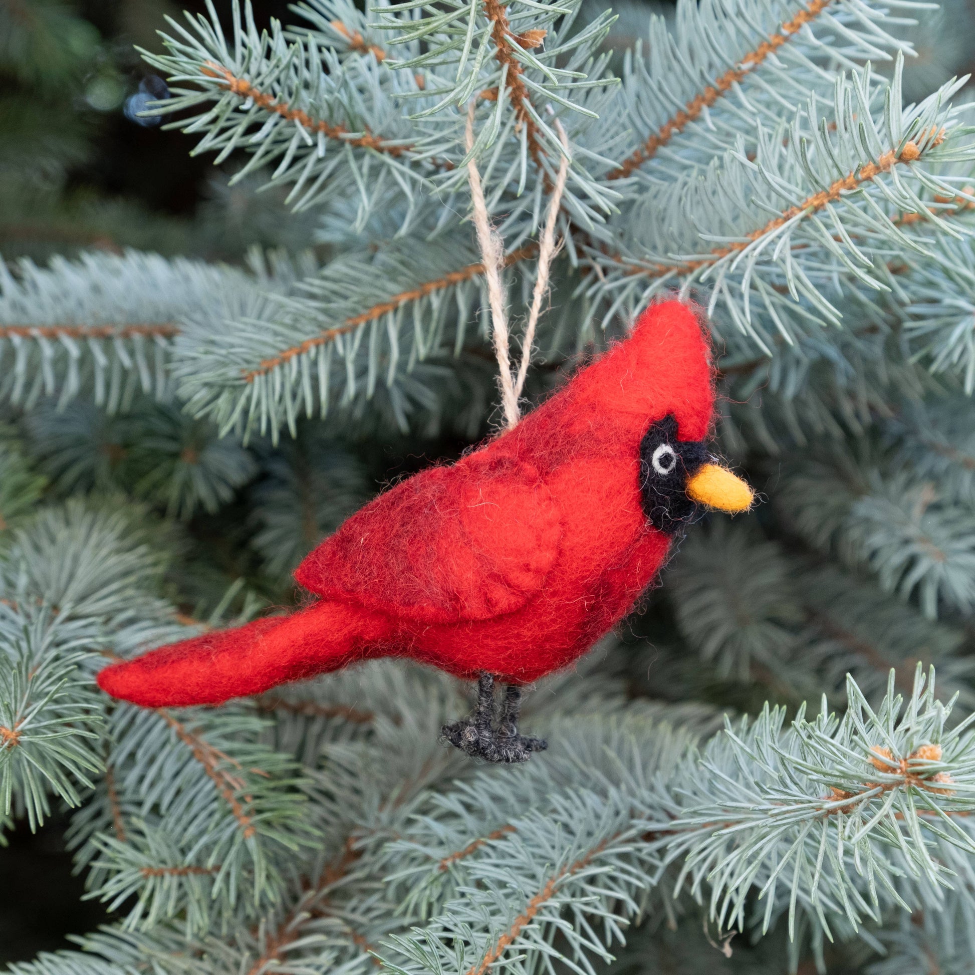 Red cardinal ornament on a branch of a pine tree