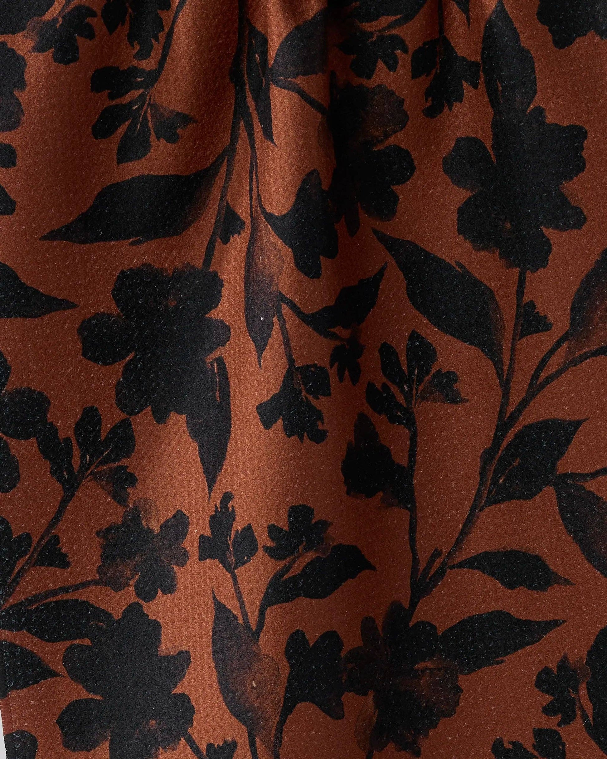 A close-up of a rust-orange fabric with a black floral and leaf pattern.